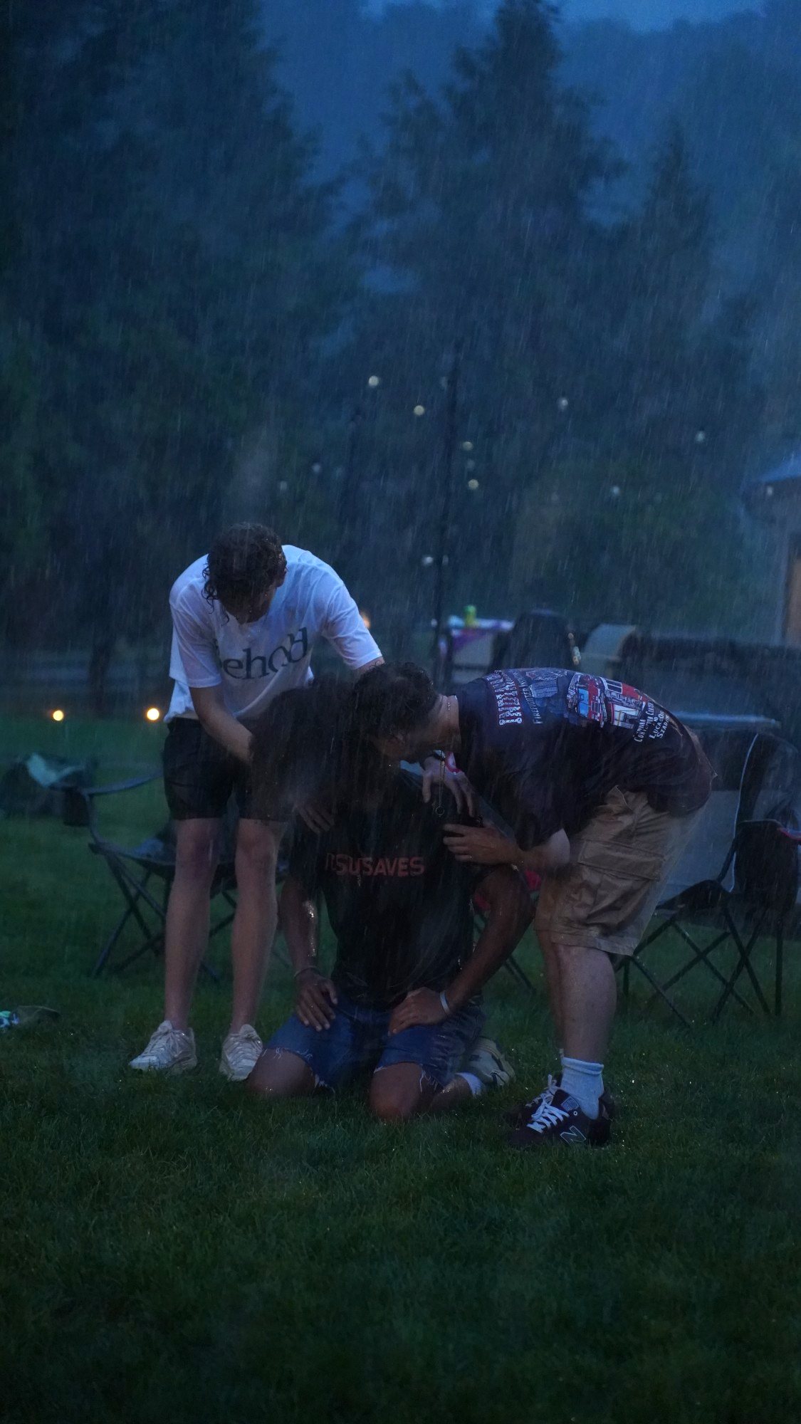 Two worshippers laying hands in prayer over a kneeling friend in the pouring rain